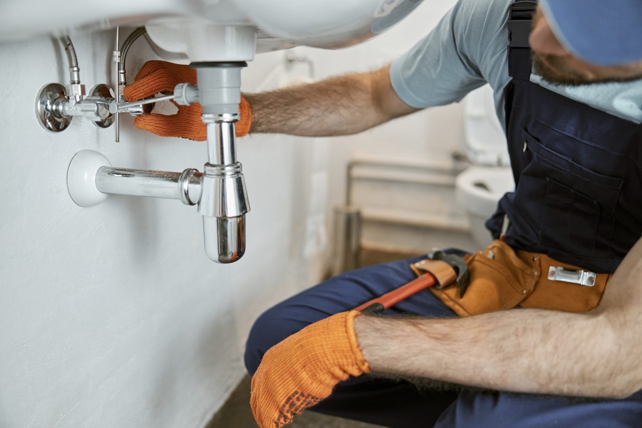 Male plumber is repairing faucet of a sink at bathroom. Good quality plumbing company service